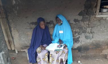 Aishatu sits with her daughter, Ummi, on a bench as they go through the Women for Women International handbook