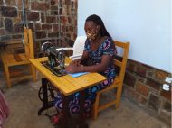 Jeanette, a graduate of Women for Women International, wears a mask while sitting at her sewing machine to create more masks