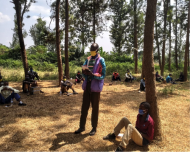 One man stands in a circle of other men, attending the Men's Engagement Program in Rwanda. They are all wearing masks created by women graduates of the signature program at the Women's Opportunity Center