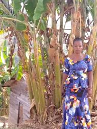 Elizabeth, a participant of Women for Women International - DRC, stands in front of trees in a patterned blue dress