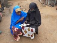 Aishatu and her daughter, Ummi, sit on the ground as Aishatu teaches Ummi different lessons