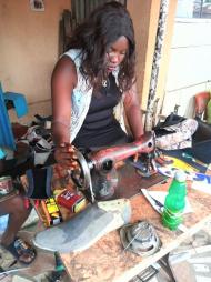 Saratu's daughter sits at a work bench and makes shoes
