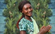 Image of a woman from Rwanda in bright clothing in front of a wreath; Photo credit: Mark Darrough