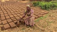 Cinama kneels on the ground next to many bricks 