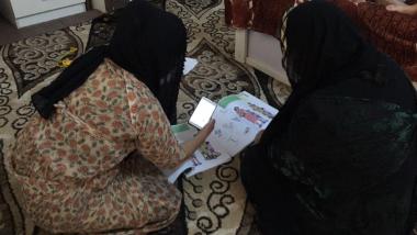 Woman sitting on floor looking at her workbook for Women for Women International online trainings in Iraq
