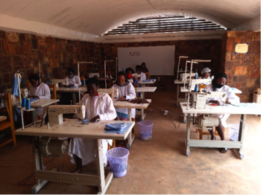 In a room at the Women's Opportunity Center in Rwanda, women sit at sewing machines spaced apart for social distancing and sew masks