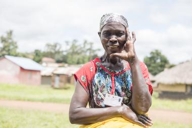 Sarah smiles at the camera, holding her hands to her face. Photo credit: Charles Atiki Lomodong