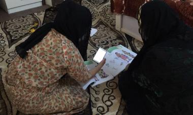 Woman sitting on floor looking at her workbook for Women for Women International online trainings in Iraq