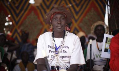 A South Sudanese woman at the Join Me on the Bridge event looks into the camera with a white shirt that seems to read, "Unity, Peace, Prosperity, and Development"