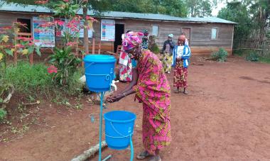 Participants in the DRC line up to use a the blue handwashing station