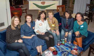 Photo of six women on a couch, smiling at the camera, with a poster of the Women for Women International logo behind them. Photo provided by Liliana Soroceanu