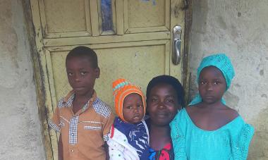 Saratu's children stand around her, as she kneels and smiles to the camera