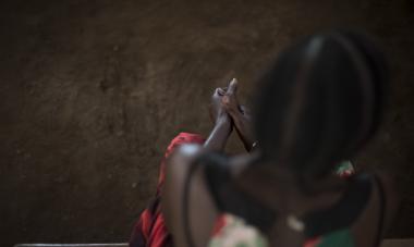 Over the shoulder shot of a woman in South Sudan sitting, with the focus on her hands. Photo credit: Charles Atiki Lomodong