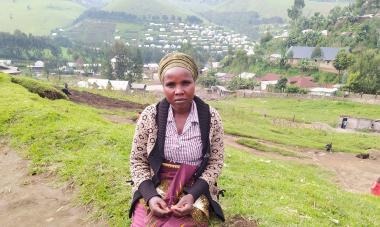 Zawadi from Rubaya, North Kivu - Democratic Republic of the Congo - looks at the camera while sitting on a green field