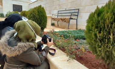 Woman crouches in front of a plant with a camera, poised to take a photo