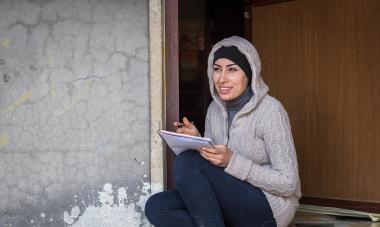 A Syrian Woman is writing in a notebook.