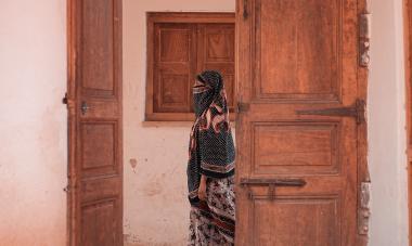 A woman walks alone past an empty room. 