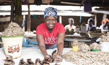 Alice smiles up at the camera from her stall, where she sells fish; Photo credit: Charles Atiki Lomodong