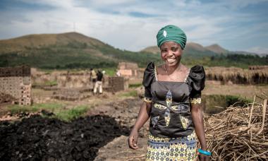 A woman, Cinama, stands and smiles proudly. Behind her is a foundation of bricks