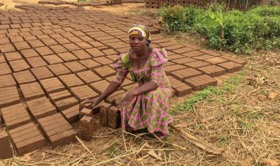 Cinama kneels on the ground next to many bricks 