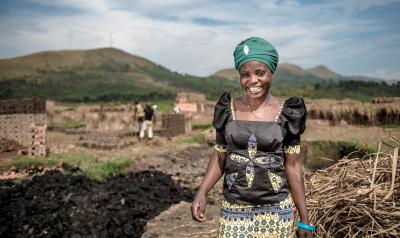 A woman, Cinama, stands and smiles proudly. Behind her is a foundation of bricks