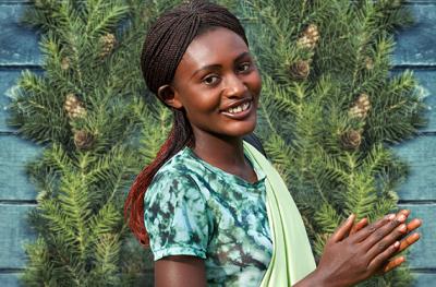 Image of a woman from Rwanda in bright clothing in front of a wreath; Photo credit: Mark Darrough